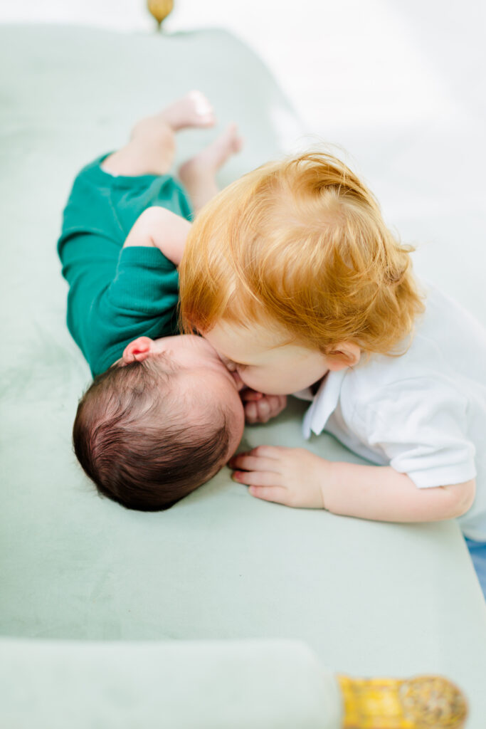 older brother kisses baby brother in newborn photo session at the oak atelier