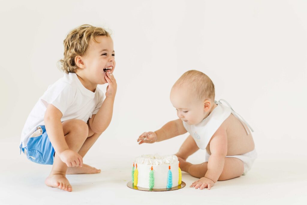 brother and baby enjoy cake smash together for baby first birthday photo shoot