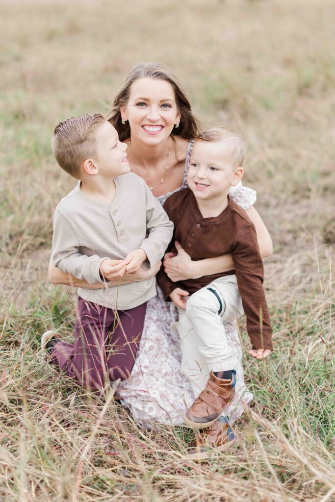 mom and two boys snuggle in an open field for houston fall mini photo shoot