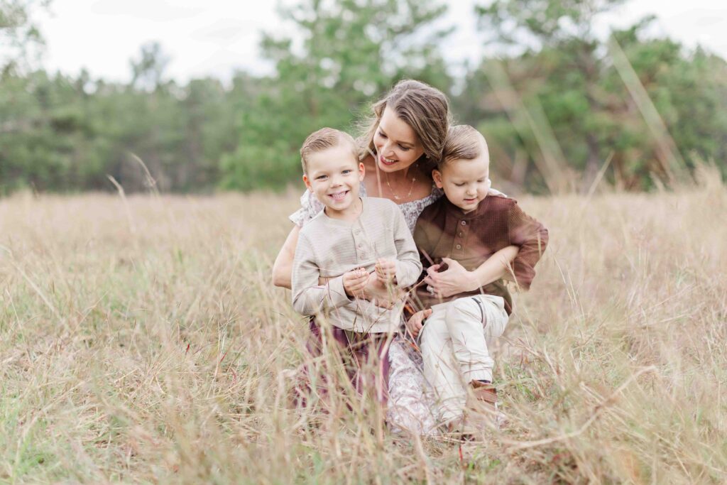 Mom and two boys snuggle in a field for family portrait session