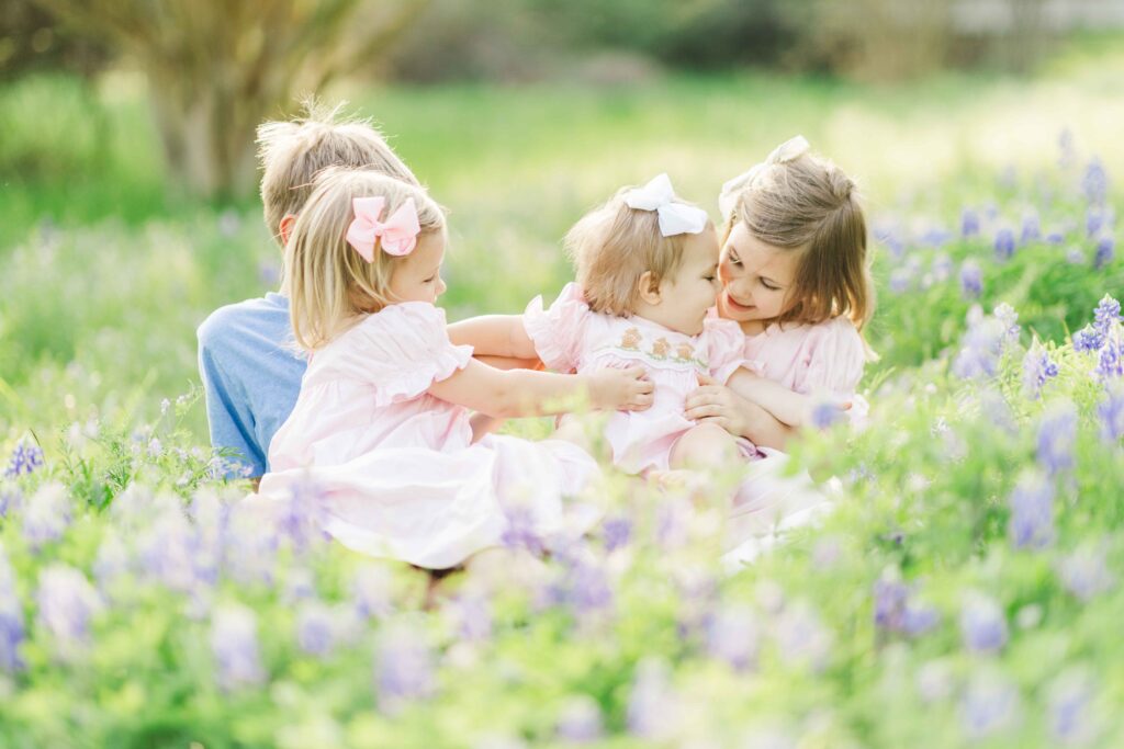 group of four siblings tickle baby sister in bluebonnet patch in houston, texas