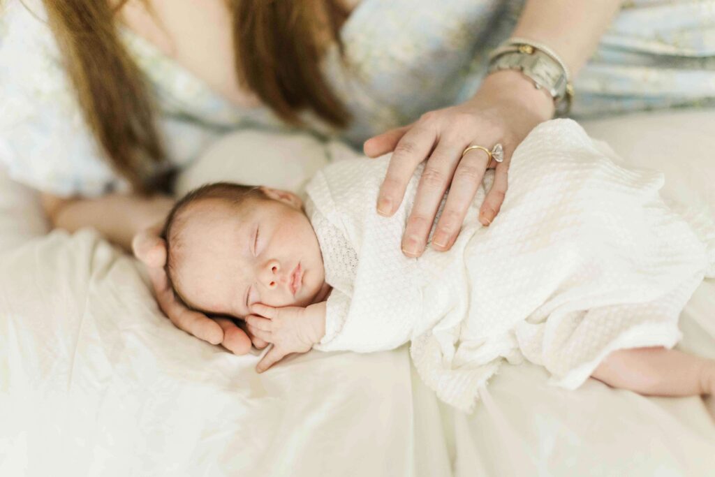 Mom snuggles baby in her hands laying on the bed together in their home for newborn photos