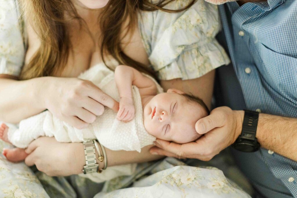 Mom and dad hold their baby together hands caressing her little body for in home photos