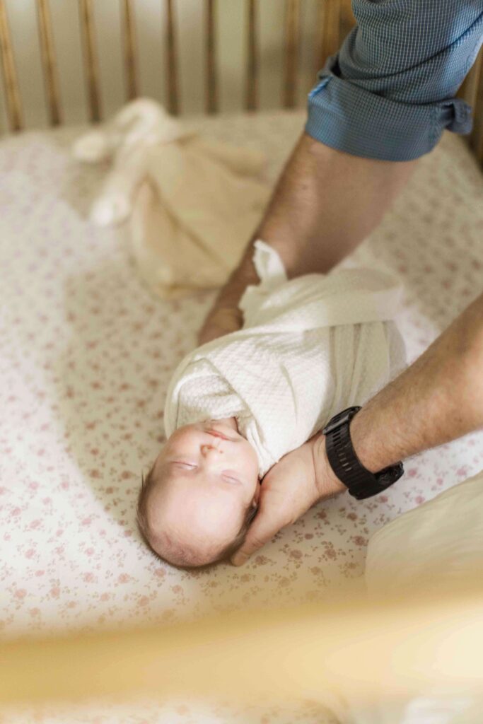Baby girl is placed in her pink floral crib swaddled in a white blanket