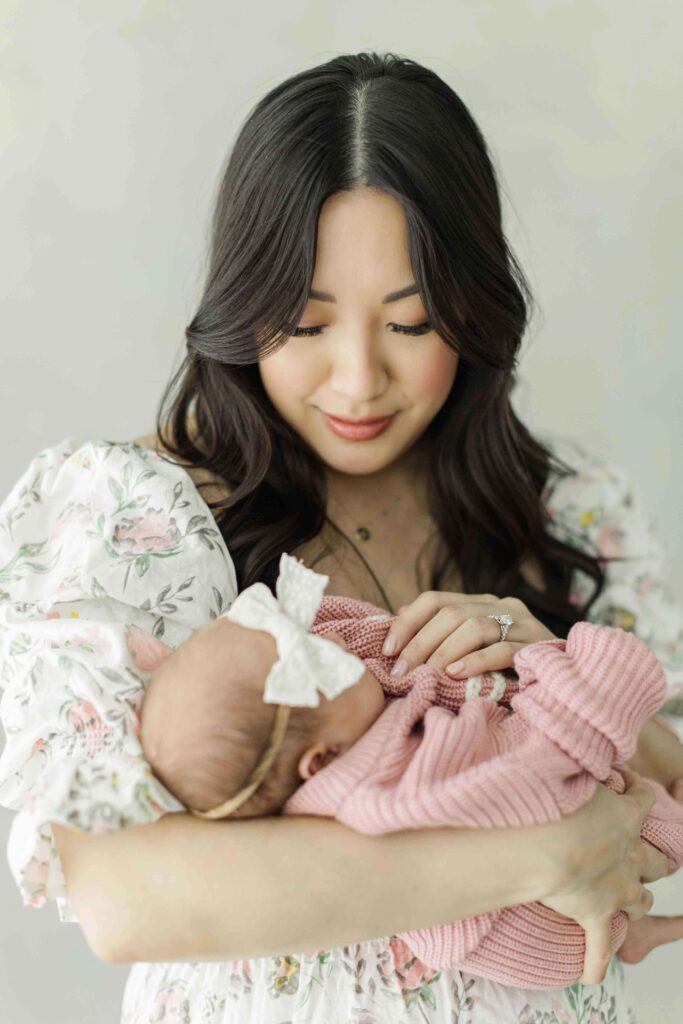 Mom holds newborn baby girl close in houston baby studio wearing a floral dress