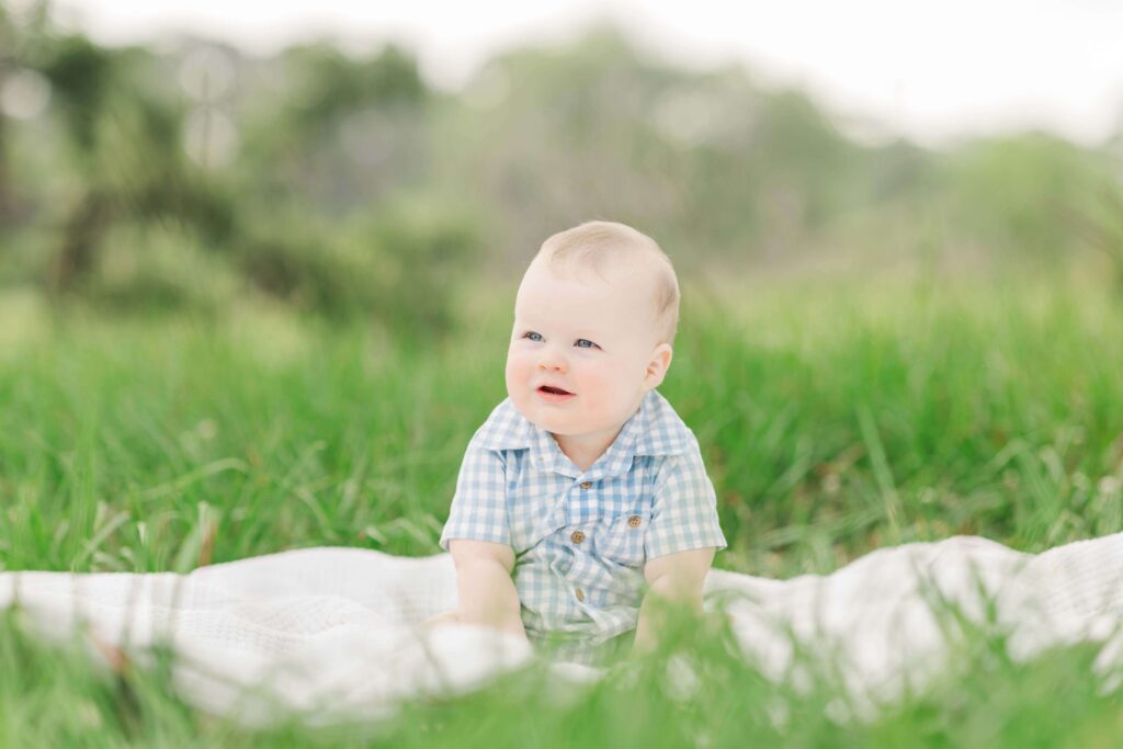 baby plays on a blanket in a wide open grassy field