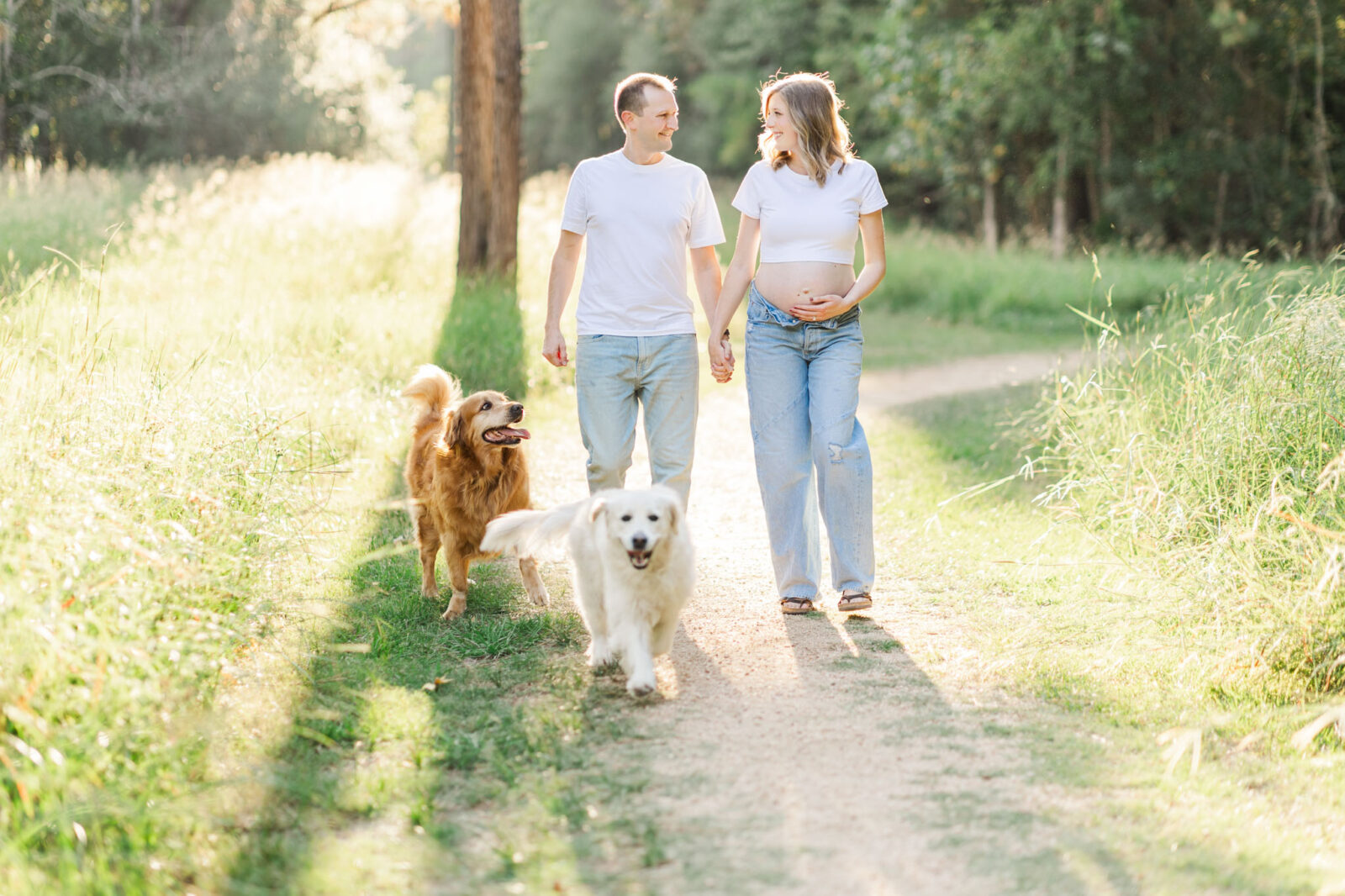 Pregnant mother standing on a sunlit trail with her partner holding hands during a maternity photoshoot in Houston.