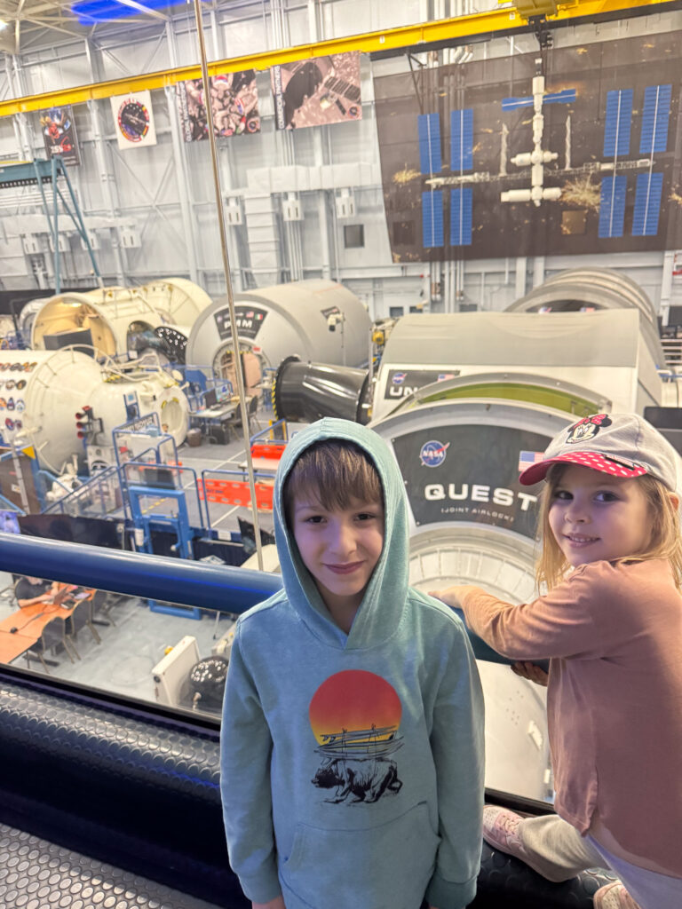 two kids smile together at houston space museum in front of rocket gear